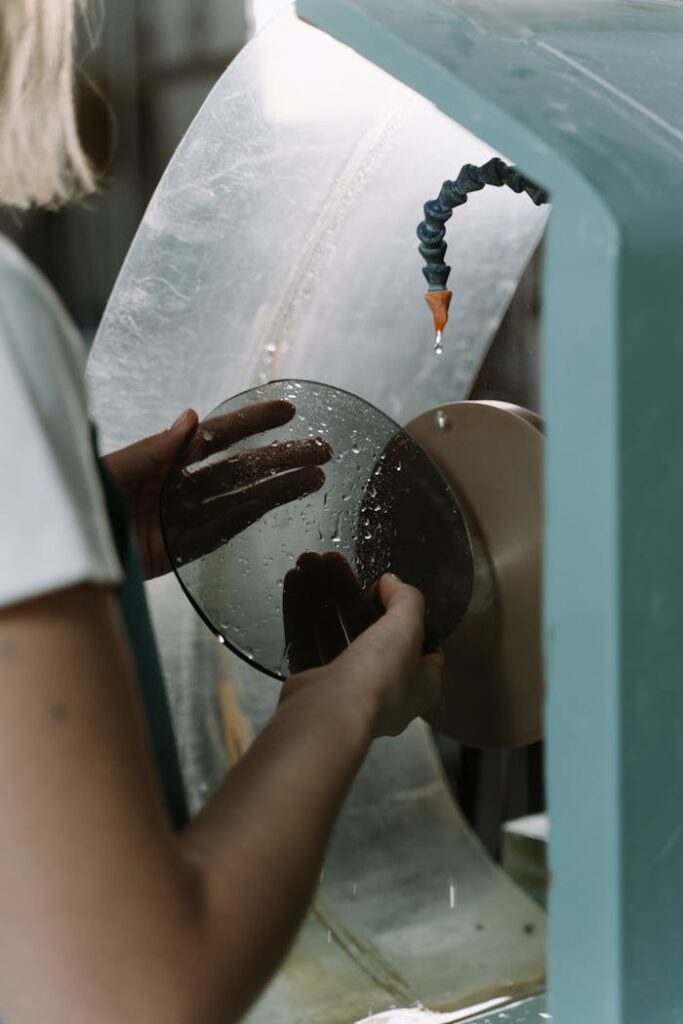 Worker using machine to cut and shape glass. Industrial craftsmanship captured in detail.